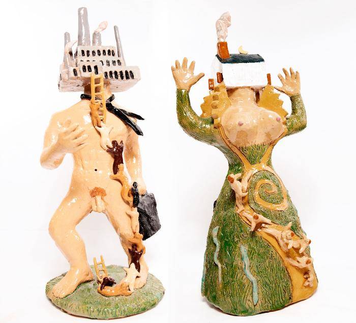 Two ceramic statues, one is a nude man with a factory in place of a head, he carries a briefcase. The is a nude woman and with a house in place of a head.